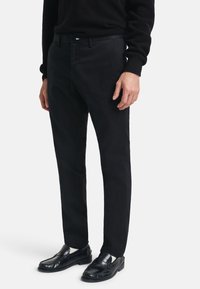 Pantalones negros de una tela suave, diseño ajustado con pierna recta, con una cintura clásica, combinados con mocasines negros.