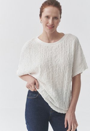 Hvid, struktureret bluse med kortærmer og bred udskæring, stylet med mørke denimjeans. Stoffet har et krøllet udseende.