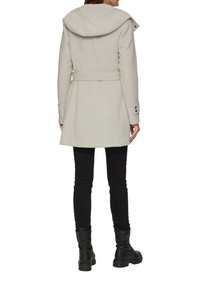 Manteau gris clair avec une grande capuche, taille ceinturée et poignets boutonnés. Pantalons noirs et bottines complètent la tenue. Texture lisse.