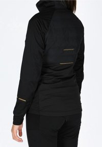 Veste isolante noire à col montant, avec des accents dorés, un design élégant et un panneau arrière texturé. Convient pour un usage extérieur.