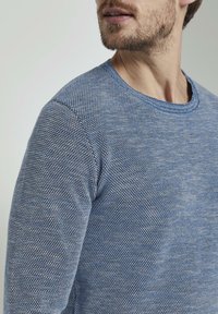Maglione blu lavorato a maglia con motivo a nido d'ape texturizzato. Scollo e polsini a costine con vestibilità rilassata. Materiale morbido evidente nella trama.