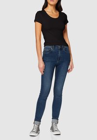 T-shirt nera a maniche corte abbinata a jeans skinny blu scuro, con taglio aderente e risvolti, indossata con sneakers alte grigie.
