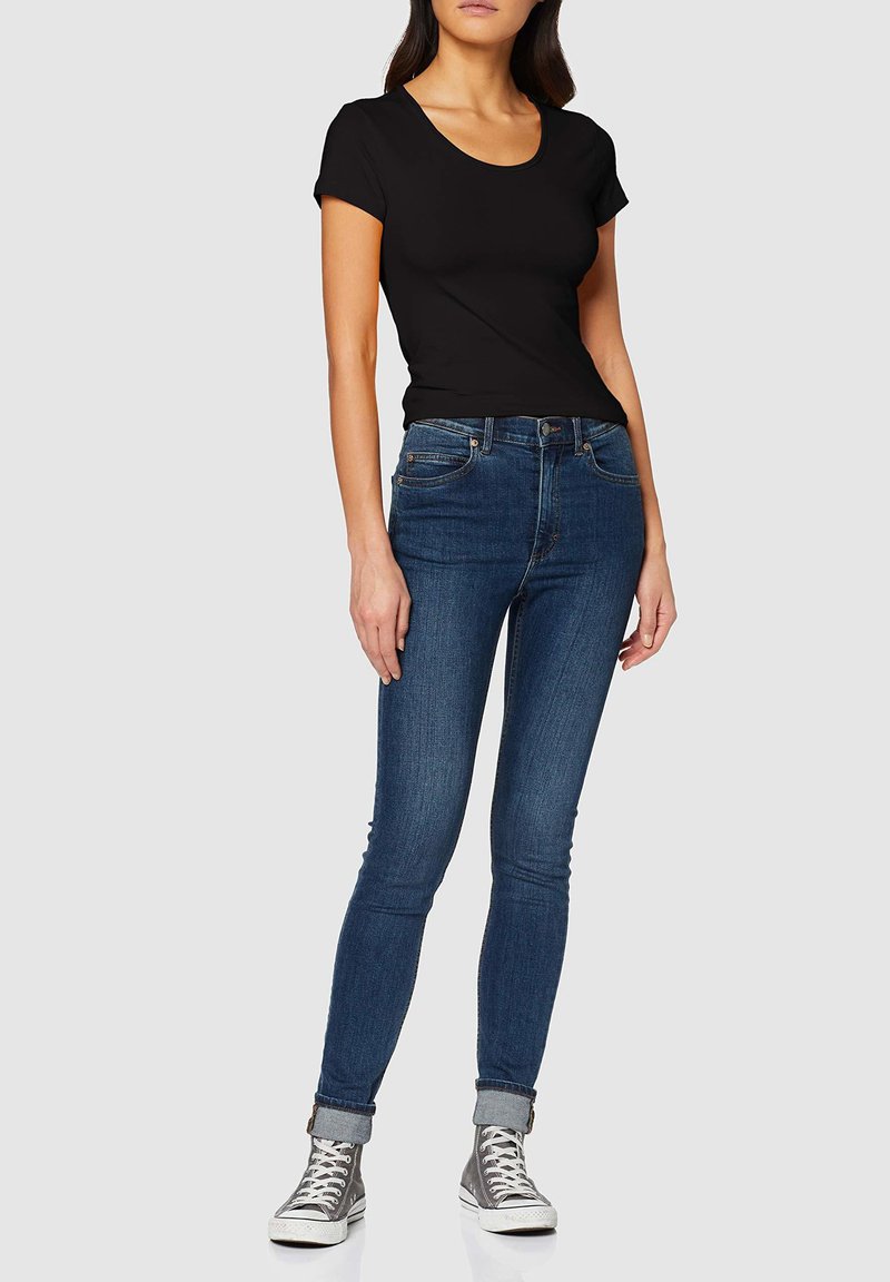 T-shirt nera a maniche corte abbinata a jeans skinny blu scuro, con taglio aderente e risvolti, indossata con sneakers alte grigie.