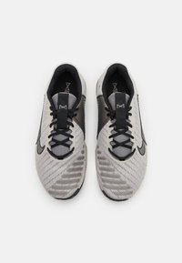 Nike sportbačiai, turintys tinklelio viršutinę dalį pilkos ir juodos spalvos, tekstūruotą dizainą, juodas raišteles ir išsiskiriantį logotipą šone.