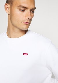 Witte sweatshirt van katoen met een ronde hals. Heeft een klein rood Levi's logo op de borst. Glad materiaal.