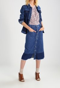 Denimjakke og nederdel med blomstermønstret bluse. Nederdelen har frontlukning med knapper og to oversize lommer. Brune ankelstøvler.