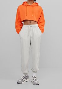Orange cropped hoodie med dragsnoddar, parr med ljusgrå sweatpants som har elastisk midja och ankle cuffs. Svarta och grå sneakers.