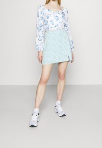 Květinový crop top s nafouknutými rukávy v bílé a modré barvě; mátově zelená mini sukně s drobným květinovým vzorem a bočním rozparkem; doplněno bílými teniskami.