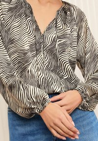 Black and white striped blouse with a drawstring neckline, gathered cuffs, and lightweight, textured fabric. Worn with blue denim jeans.