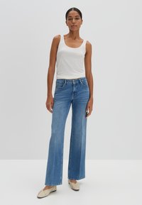 Strakke witte tanktop gecombineerd met lichtblauwe wijde jeans, met een knoopsluiting aan de voorkant en gestikte details. Platte schoenen maken de look af.