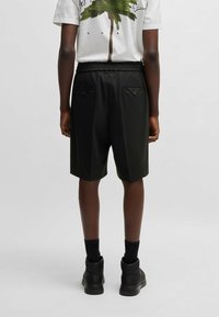Black shorts with an elastic waistband, two back pockets with flaps, and a loose fit. Paired with a white graphic t-shirt and black boots.