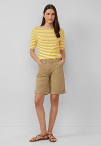 Haut à manches courtes rayé jaune et blanc, associé à un short kaki mi-cuisse. Sandales avec des lanières marron. Tenue simple et décontractée.