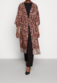 Kimono w wzór paisley w kolorze koralowym i czarnym, z przewiązywaniem w talii, rękawami 3/4 oraz misternym detalem na brzegu. Nosi się go na czarnym stroju.