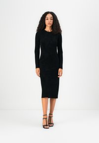 Must be musto ja pikkade varrukatega kleit, millel on tekstuuriga kangas, mid-calf pikkus ja keha tutvustav siluett. Kombineeritud mustade rihmadega kontsakingadega.
