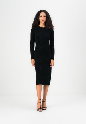 Black long-sleeve dress made of textured fabric, mid-calf length, fitted silhouette. Paired with black strappy heels.