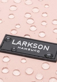 Rózsaszín anyag, kiemelkedő, kör alakú vízcseppekkel, fekete címkével, rajta fehér felirattal: "LARKSON HAMBURG." Sima textúra és modern dizájn.