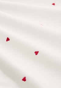 Λευκό ύφασμα με μικρές, ομοιόμορφα κατανεμημένες κόκκινες καρδιές κεντημένες σε όλη την επιφάνεια.