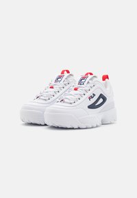 Baskets blanches avec une semelle épaisse, comportant un accent gris foncé et un marquage rouge et bleu. Semelle extérieure crantée pour l'adhérence.