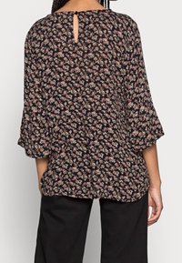 Blouse fleurie à manches trois-quarts, base noire avec petites fleurs multicolores, détail dos en trou de serrure, tissu léger, coupe décontractée.
