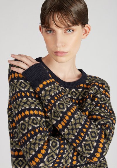 Sweter dzianinowy z ciemnonavybą bazą w geometryczne wzory w kolorze pomarańczowym, zielonym i białym. Ściągacze przy rękawach i okrągły dekolt. Teksturowane wykończenie.