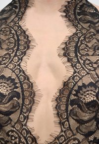 Βαθύ ντεκολτέ σε σχήμα V με περίτεχνο ύφασμα από μαύρη δαντέλα που διαθέτει λουλουδάτα και γεωμετρικά μοτίβα πάνω σε γυμνό δέρμα.