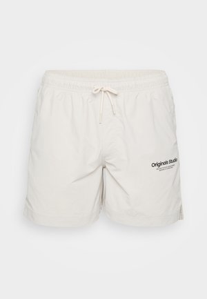 Light beige shorts made of soft fabric, featuring an elastic waistband with drawstring and a printed "Originals Studio" logo on the front.