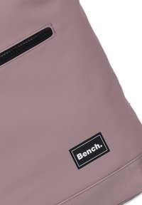 Roze waterdichte stoffen tas met een ritsvak, met een zwart 'Bench.' logo label en een gladde textuur.