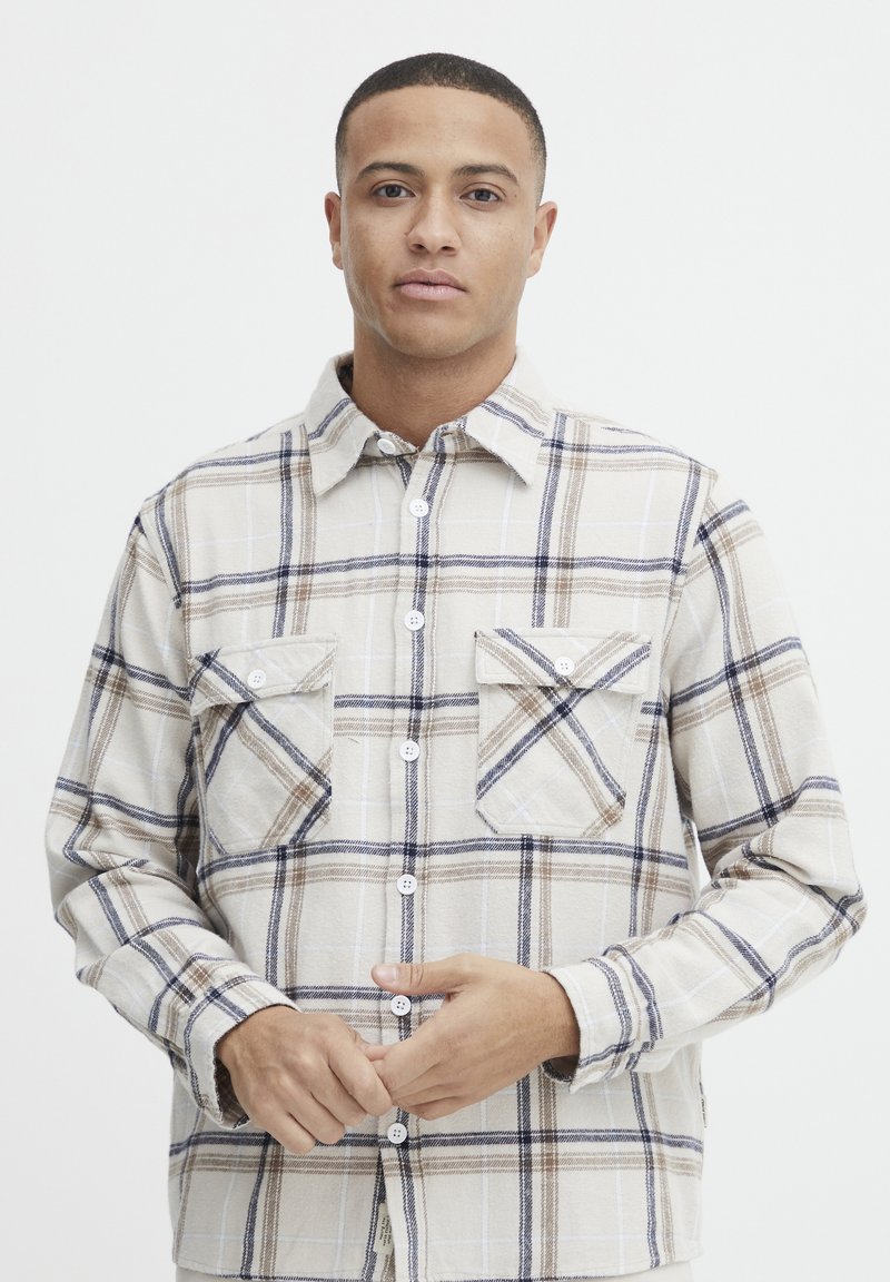 Geruite blouse in crème, bruin en marineblauw. Heeft twee borstzakken, een kraag en een gestructureerde stof.