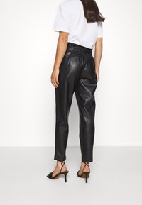 Svarta byxor i konstläder med en avsmalnande design, hög midja och elastisk midja. Kombineras med svarta klackar med remmar.