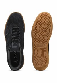 Svarta mockaskor med en texturerad ovandel, som har gummisula med rundmönster och flätade snören, prydda med Puma-loggan.