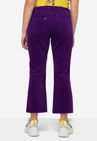 Lila kordfärgade byxor med en utfläkt design, med midjeband, två bakfickor och råa fållar. Bärs med flerfärgade sneakers.