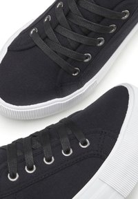 Juodos drobės sportbačiai su plokščiomis juodomis raištelėmis, sidabriniais akmenukais ir balta guma padu su tekstūruotu raštu.