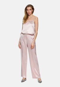 Pink satin camisole paired with wide-leg trousers, featuring a soft sheen and delicate straps. Complemented by light gray loafers.