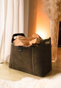 Ciemnobrązowy zamszowy kosz na drewno do kominka z zaokr�ąglonymi krawędziami i bocznymi uchwytami, wypełniony ułożonym drewnem opałowym. Widoczny charakterystyczny detal w postaci szwów.