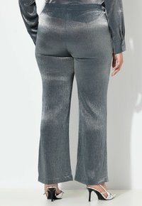 Lichte metalen zilveren uitlopende broek met een glanzende textuur. Beschikt over een aansluitende taille en een subtiele glans, wat bijdraagt aan een slanke silhuet.