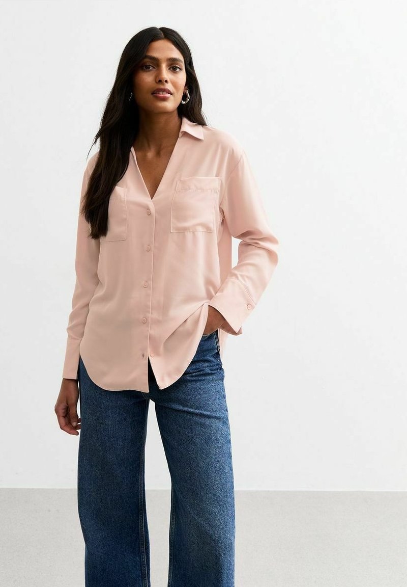 Lichtroze blouse met lange mouwen, kraag, notch-neklijn, enkele borstzak en knopen aan de voorkant, gecombineerd met donkerblauwe wijde jeans.