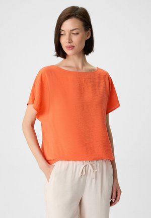 Orange short-sleeve top with a loose fit and a wide neckline, made from lightweight fabric, paired with light beige drawstring pants.