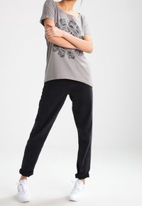 Camiseta gris de manga corta con un diseño floral negro, combinada con pantalones negros con dobladillo y zapatillas blancas. Líneas modernas y limpias con un ajuste casual.