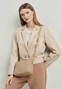 Beżowa skórzana torebka na ramię z złotymi akcentami, prostokątnym kształtem i gładką fakturą, uzupełniona regulowanym paskiem.