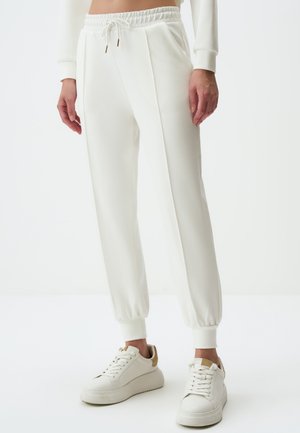 Witte joggers met een trekkoord in de taille en boorden, met een gladde textuur en subtiele zijnaad. Gepaard met witte sneakers.