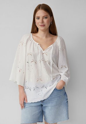 Weißes, leichtes Blusenshirt mit dekorativer Stickerei und V-Ausschnitt. Verfügt über kurze, weite Ärmel und einen lockeren Schnitt. Kombiniert mit blauen Jeansshorts.