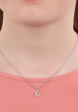 Collana d'argento con un piccolo pendente a forma di ferro di cavallo, adornato con cristalli trasparenti. Catenina fine con design a maglia, indossata su una maglietta color pesca.