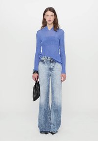 Blue knit sweater with a ribbed pattern, paired with high-waisted, wide-leg faded denim jeans. Model holds a black handbag.