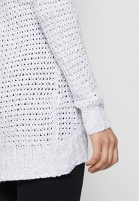 Pull blanc en tricot avec un design loose et en maille ouverte, des poignets et un ourlet côtelés, fabriqué dans un tissu texturé et respirant.
