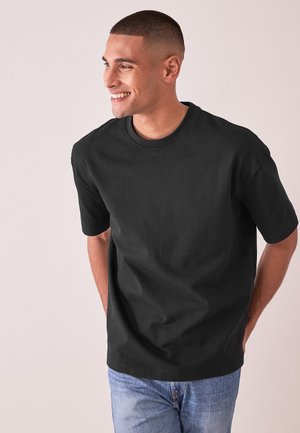 Zwart katoenen t-shirt met korte mouwen en een ronde hals, met een ontspannen pasvorm en een soepele textuur. Gekleed met lichtblauwe jeans.