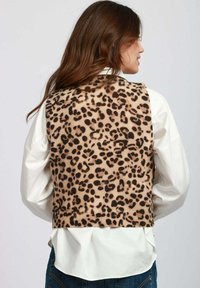 Gilet con stampa leopardata realizzato in tessuto morbido, caratterizzato da un orlo a coste, indossato sopra una camicia bianca. Il design presenta distintive macchie nere su uno sfondo beige.