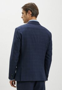 Giacca da abito blu navy con motivo a griglia, spacco singolo e dettagli a tre bottoni sui polsi. Il tessuto appare strutturato con una finitura liscia.