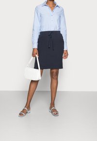 Světle modrá košilová košile, námořnická sukně na šňůrku, bílá prošívaná kabelka a světle modré sandály se čtvercovými špičkami. Jednoduchý, čistý design.