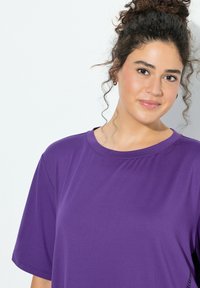 Fioletowy t-shirt o luźnym kroju z krótkimi rękawami, wykonany z miękkiego materiału. Ma zaokrąglony dekolt i subtelne przeszycia po bokach.