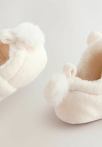 Pantoufles blanches et douces avec des accents en pompon et une forme arrondie, fabriquées en matériau pelucheux. Intérieur doublé pour un confort supplémentaire.